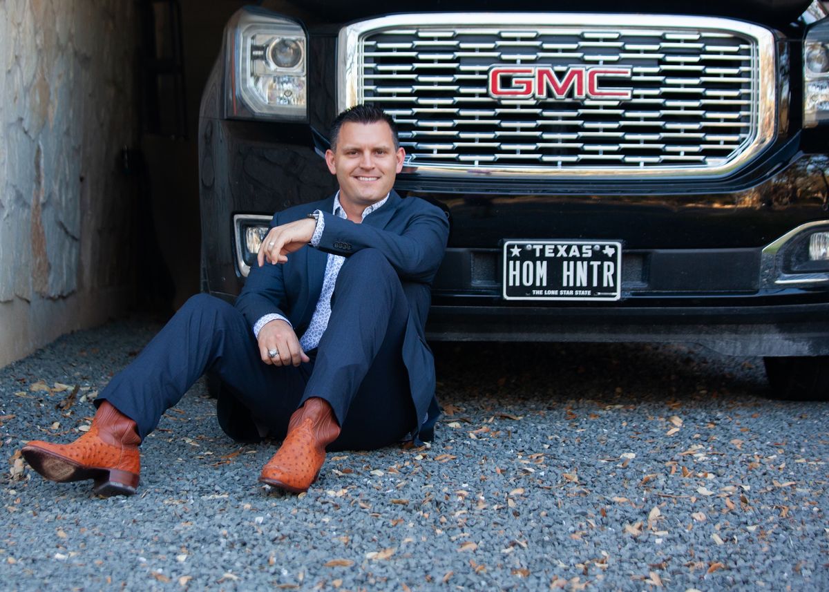 Scott McCord sitting in front of his GMC with the HOM HNTR plate